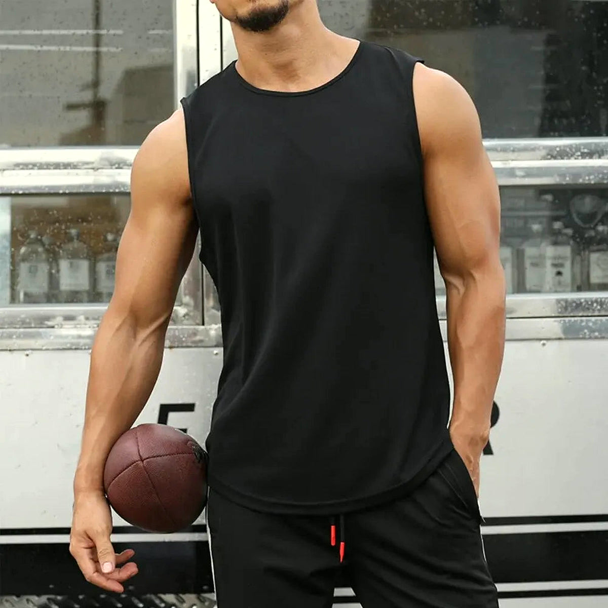PrimeBuild Men's Quick-Dry Running Tank in black on a man holding a football, showing the crew neckline and open armholes