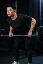 Man doing a barbell row in a gym wearing the PrimeBuild Men's Compression Training Shirt in Black