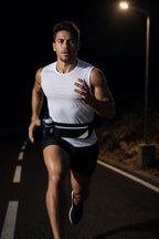 Man running on a road at night wearing the black PrimeBuild Hydration Running Belt with a bottle at his side