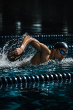 Swimmer doing freestyle in a pool lane wearing a black PrimeBuild Swim Hand Paddle