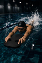 Swimmer in cap and goggles kicking in a pool lane while holding the black PrimeBuild Ergonomic Swim Kickboard