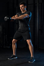 Man wearing black PrimeBuild Men's Performance Training Shorts doing a kettlebell swing in a dark gym