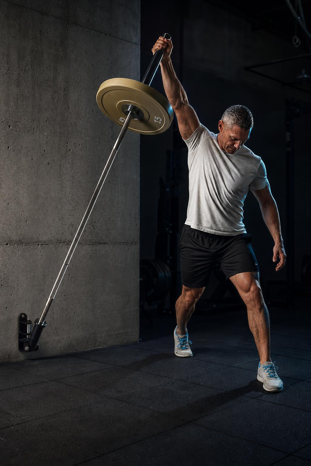 PrimeBuild Wall-Mounted Landmine Attachment on a concrete wall holding a loaded barbell during a one-arm press