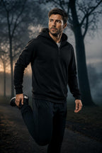 Man wearing the black PrimeBuild Men's Quarter Zip Fleece Hoodie over a white T-shirt, doing a quad stretch on a misty path