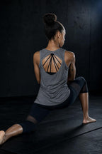 PrimeBuild Women's Open-Back Performance Tank in grey worn over a strappy sports bra during a low lunge stretch on a mat
