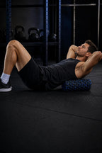 Man lying on a gym floor with the black and blue PrimeBuild High-Density Foam Roller under his upper back
