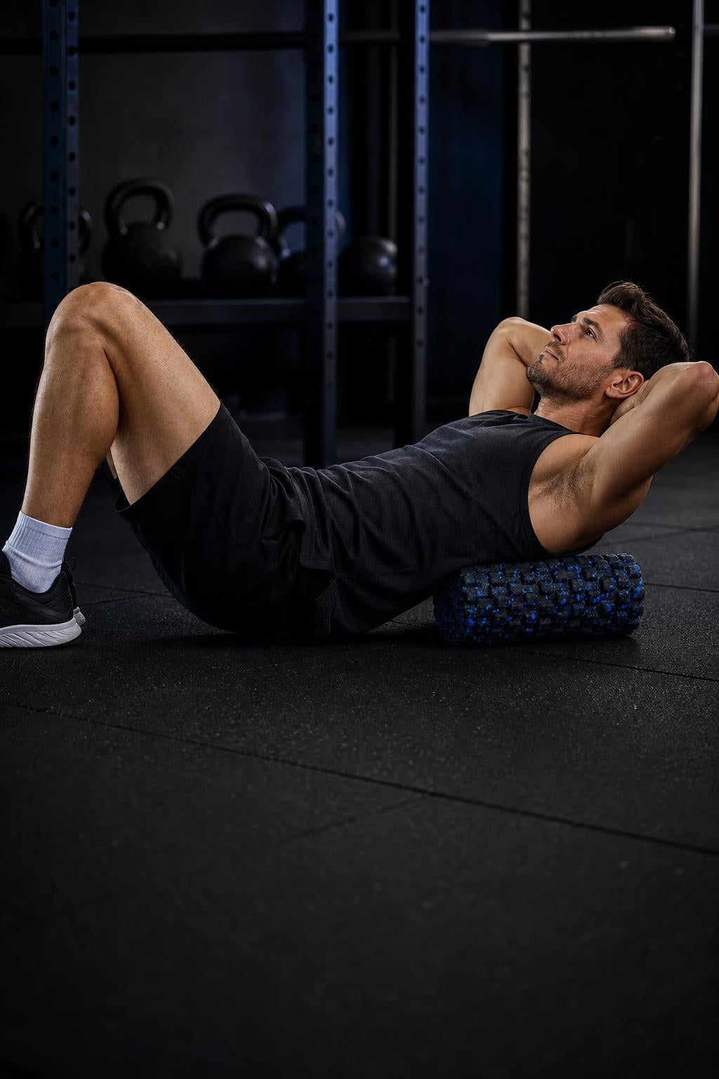 Man lying on a gym floor with the black and blue PrimeBuild High-Density Foam Roller under his upper back
