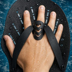 Close-up of a hand in a PrimeBuild Swim Hand Paddle, silicone finger loop on the middle finger and straps on a wet blade