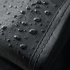Close-up of the black PrimeBuild bench cover fabric with water droplets beading beside a double-stitched seam
