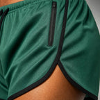 Close-up of PrimeBuild Men's Performance Running Shorts: green mesh, black-trimmed split hem and zippered pocket