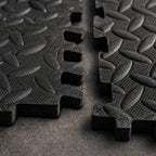 Close-up of PrimeBuild Interlocking Foam Gym Mat tiles showing black puzzle edges and diamond plate texture