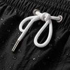 Close-up of PrimeBuild black swim trunks waistband: white drawcord, metal eyelets and water drops on the fabric