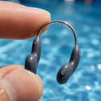 Close-up of a wet grey PrimeBuild Swim Nose Clip held between fingers, showing the thin wire and rounded pads