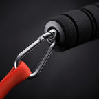 Close-up of a PrimeBuild resistance band handle with black foam grip and metal carabiner clipped to a red band